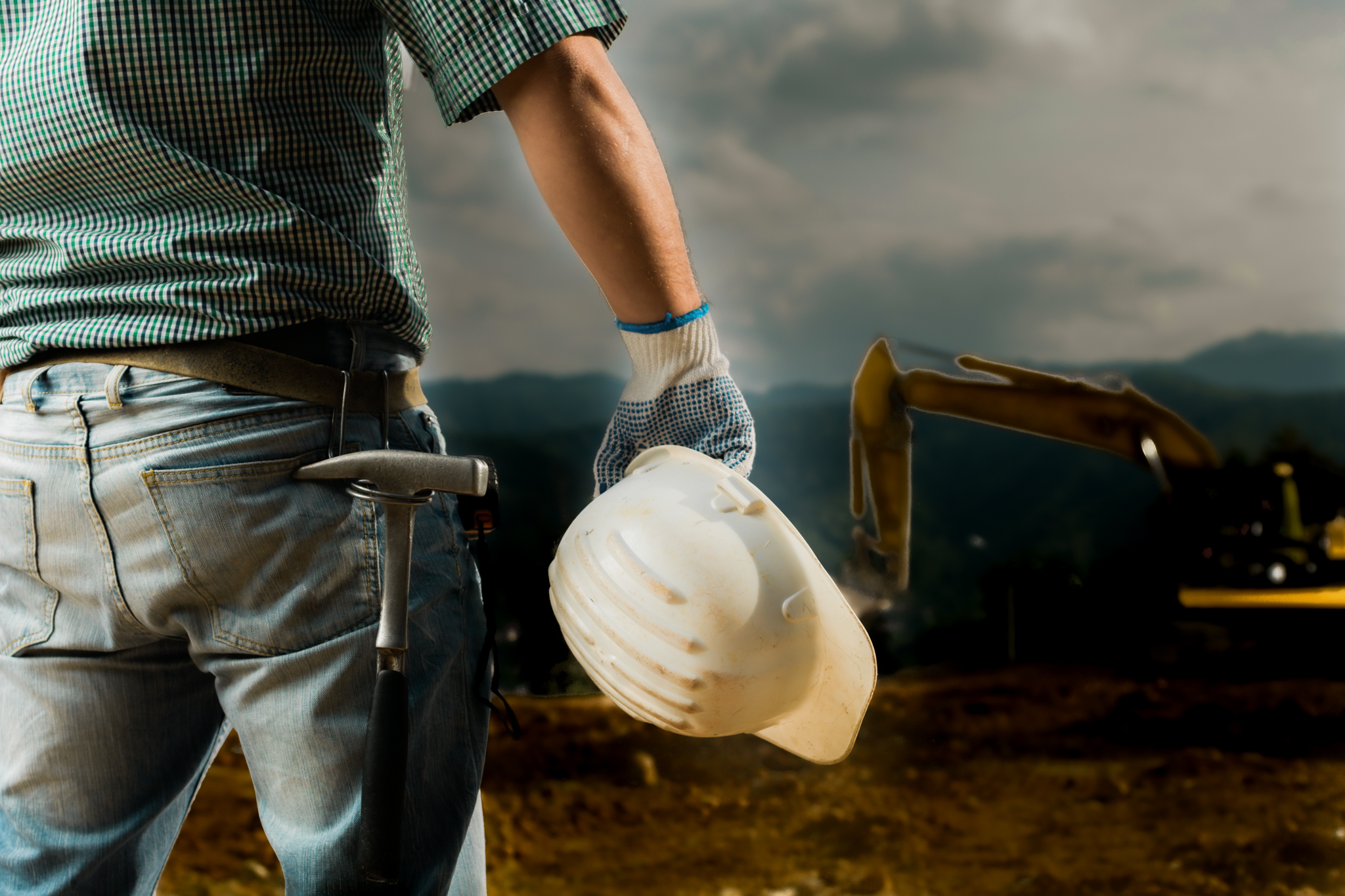 closeup back view of male engineer standing on construction site holding white hardhat